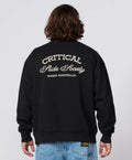 A person shown from the back wearing a black crewneck sweatshirt with 'CRITICAL Hide Society BONDE AUSTRALIA.' printed in white across the back, paired with blue jeans, against a light gray studio background.